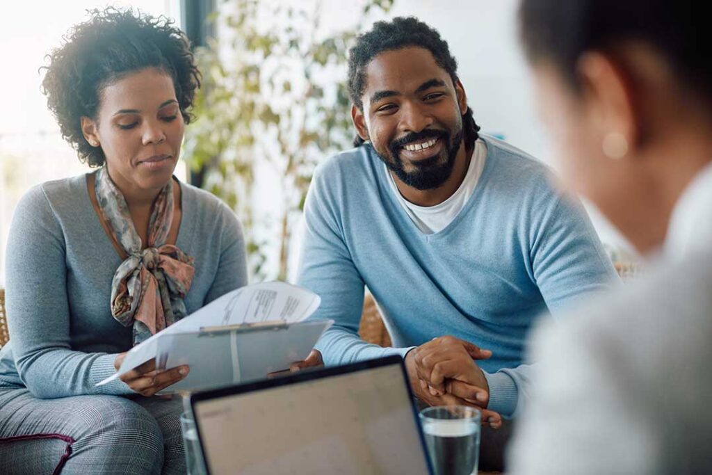 A young family with a baby sitting together at home, reviewing paperwork and discussing documents on their dining table.