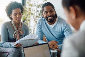 A young family with a baby sitting together at home, reviewing paperwork and discussing documents on their dining table.